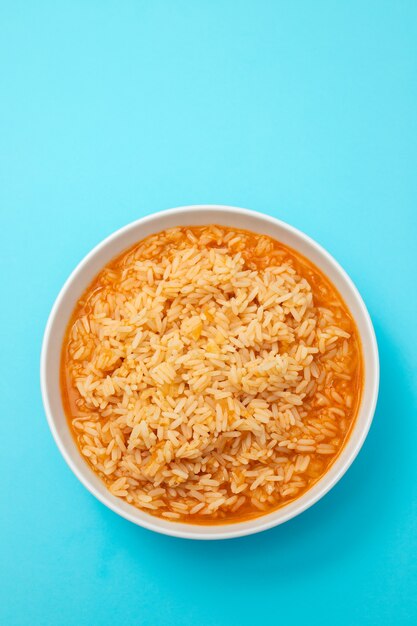 Vista superior de arroz con tomate en un tazón sobre fondo azul.