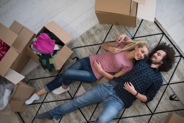 Vista superior de una atractiva pareja joven moviéndose, tomándose de la mano, mirando a la cámara y sonriendo mientras yacía entre cajas de cartón