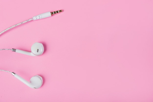 Foto vista superior de auriculares blancos con plugin sobre fondo rosa