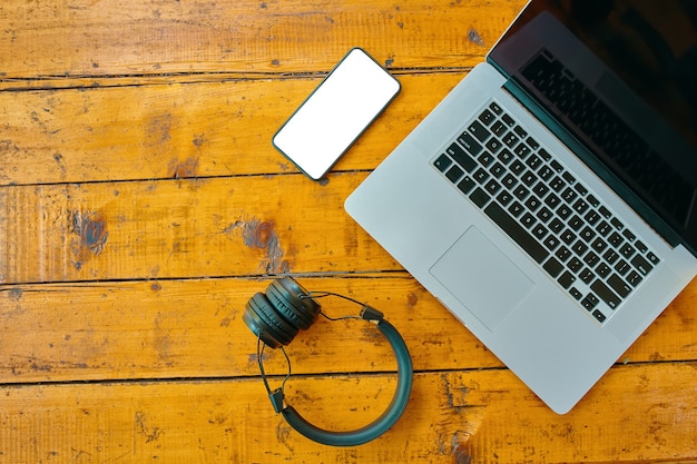 Vista superior de los auriculares inalámbricos portátiles y el teléfono móvil en la superficie de trabajo de los autónomos de mesa de madera ...