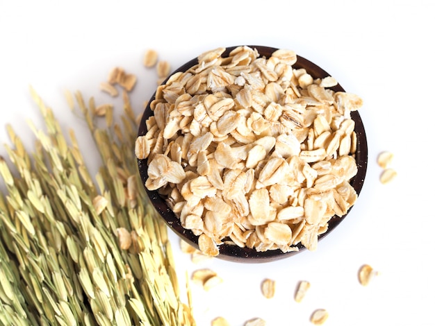 Vista superior de avena seca, avena arrollada en un tazón de madera con granos secos y espiga de arroz aislado