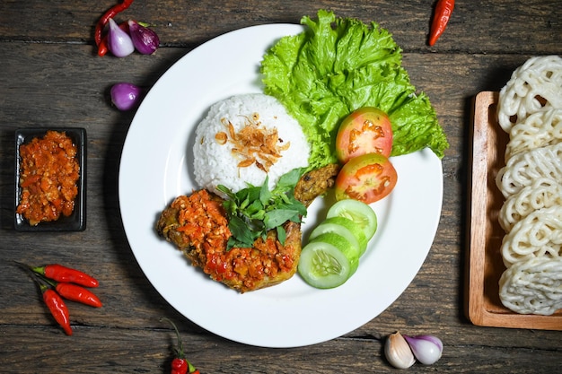 Vista superior Ayam geprek comida indonesia con salsa picante de sambal servida con arroz en un plato blanco