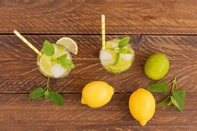 Vista superior de bebidas refrescantes de verano en mesa de madera. Enfriar limonada fresca con lima, limón, hojas de menta y hielo.