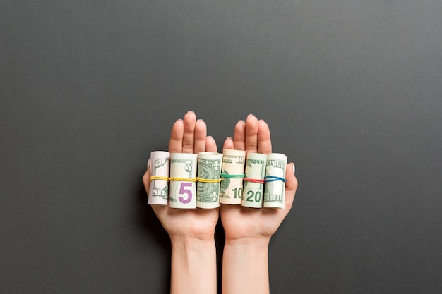 Foto vista superior de billetes de dólar enrollados en tubos en palmas femeninas sobre fondo negro