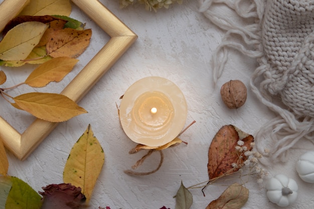 Vista superior del bodegón de la vendimia del otoño con las hojas caídas, la rosa seca, la luz de las velas y la manta tejida. Concepto de ambiente otoñal