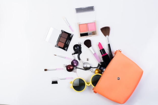 Vista superior de una bolsa de maquillaje, con productos cosméticos de belleza derramando sobre un fondo blanco.