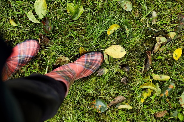 Vista superior de botas de goma rojas brillantes en la hierba con hojas de otoño