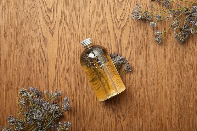 Vista superior de la botella transparente con producto de belleza natural cerca de hierbas secas sobre fondo de madera