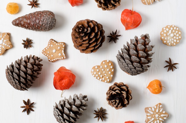 Vista superior brillante Diseño de Navidad con galletas de jengibre, piñas y physalis naranja sobre una mesa de madera blanca.