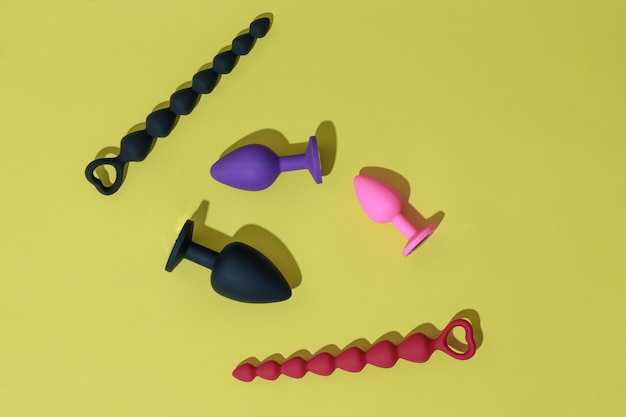 Vista superior de buttplugs y consoladores para sexo anal sobre fondo amarillo con concepto de sex shop de sombras