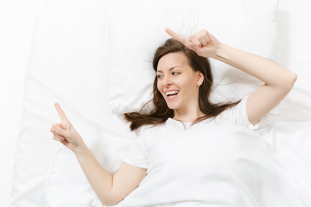 Vista superior de la cabeza de la mujer joven morena feliz acostado en la cama con sábana blanca, almohada, manta