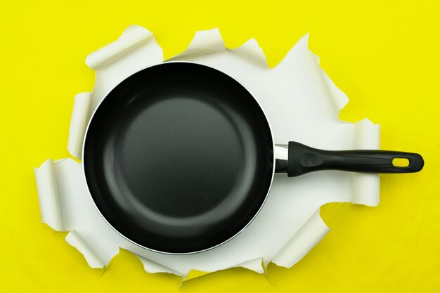 Vista superior de la cacerola de utensilios de cocina en papel rasgado amarillo.
