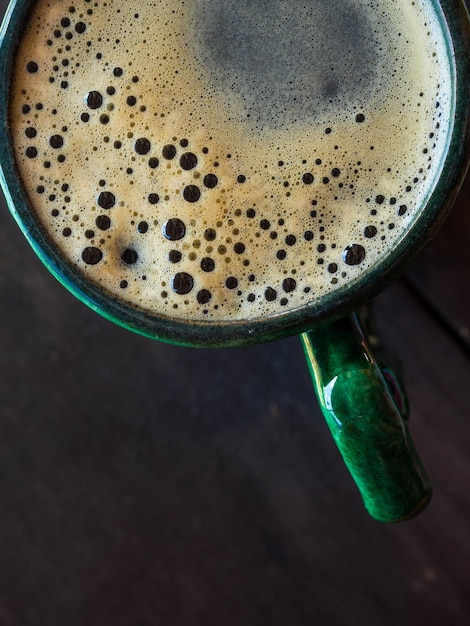 Vista superior de café caliente en taza verde sobre fondo de madera