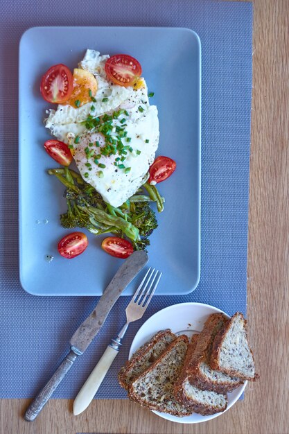 Vista superior café da manhã, ovos fritos com brócolis assado, tomate, pão integral