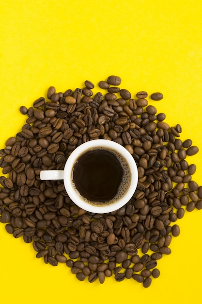 Vista superior de café negro en la taza blanca y granos de café sobre superficie amarilla