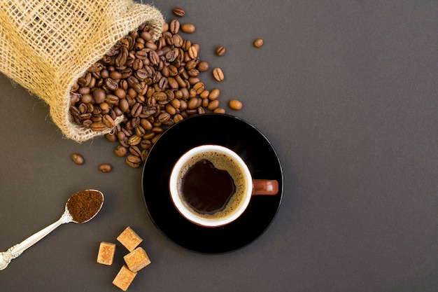 Vista superior del café negro en la taza marrón y granos de café sobre el fondo oscuro