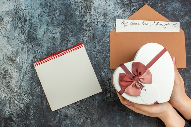 Vista superior caixa em forma de coração em mãos femininas caderno de cartas de amor em fundo escuro