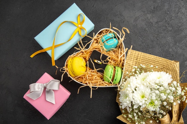 Vista superior de la caja en forma de corazón con macarons anillo de compromiso regalos ramo de flores en la mesa