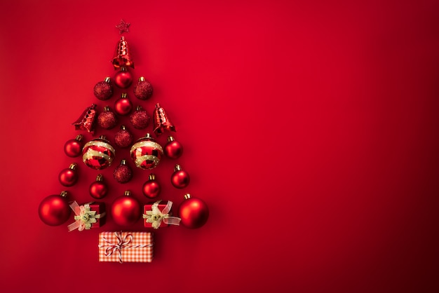 Vista superior de la caja de regalo con la bola roja y la campana en la forma del árbol de navidad en fondo rojo.