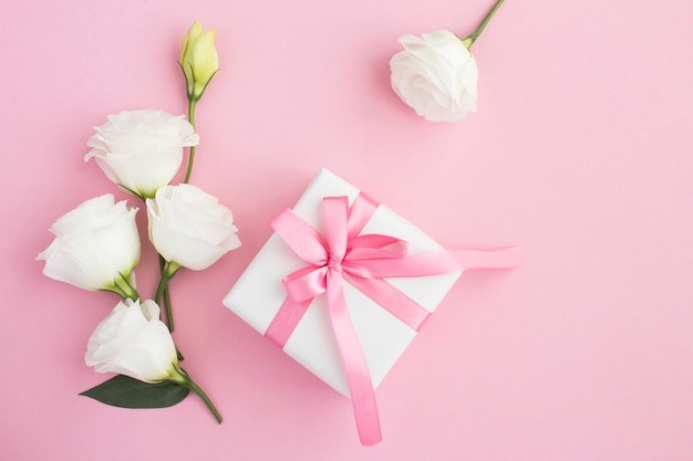 Vista superior de la caja de regalo, flores blancas y rosadas en la mesa rosa