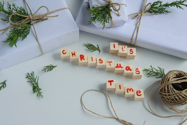 Vista superior de cajas de regalo artesanales blancas con su tiempo de Navidad letras de madera de texto y salvado de abeto fresco