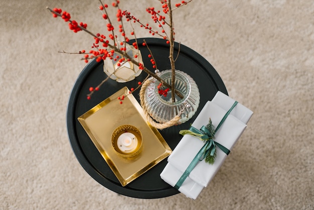 Vista superior de cajas de regalo atadas con una cinta de esmeralda con una ramita de abeto, una vela, un jarrón de bayas rojas y una bandeja de oro.