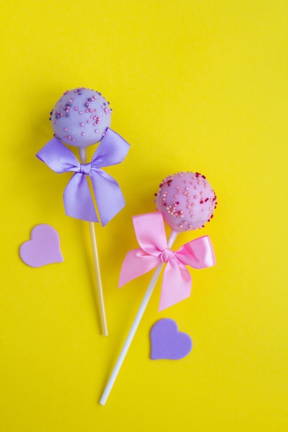 Vista superior de cake pops con arcos rosas y violetas en la superficie amarilla