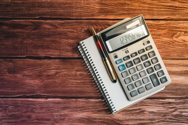 Vista superior de una calculadora con un bolígrafo y un cuaderno en una mesa de madera rústica Concepto de educación en finanzas empresariales