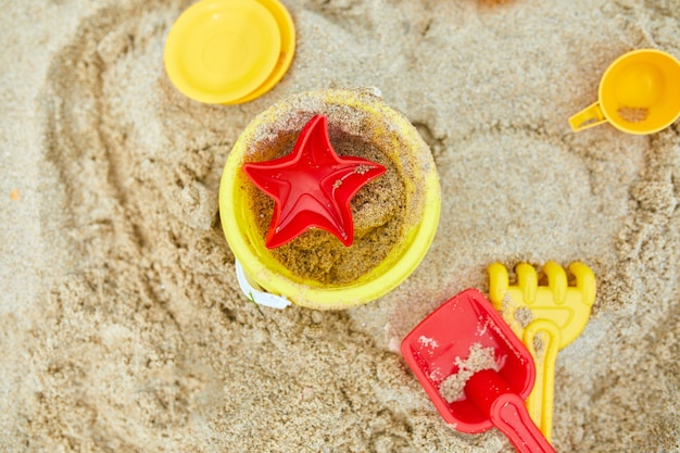 Vista superior, camada plana de brinquedos de praia de plástico espalhados no fundo de areia, férias de verão em família