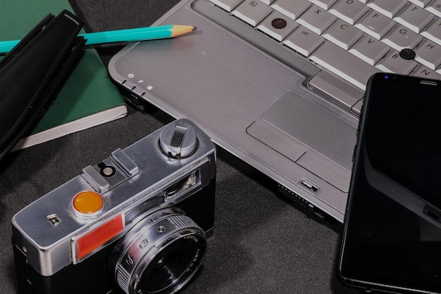 Vista superior de una cámara de fotos, una computadora portátil, un bloc de notas en blanco con un lápiz verde y un teléfono celular en un gra