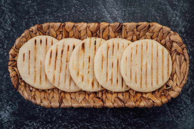 Vista superior de la canasta tejida llena con un grupo de arepas latinoamericanas sobre un fondo oscuro