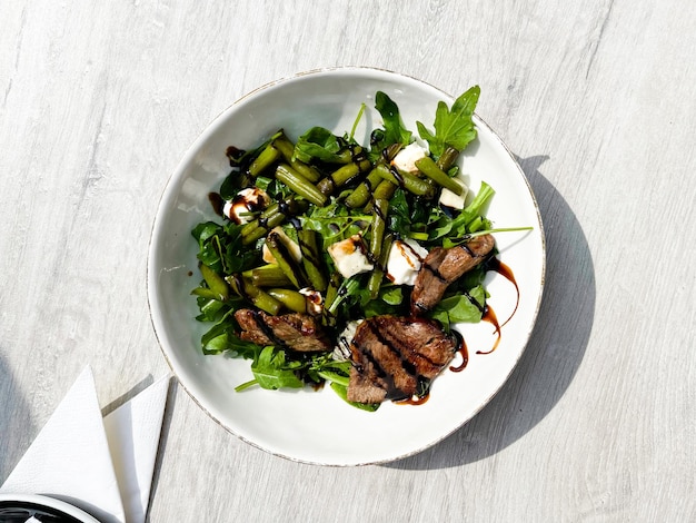 Vista superior de la carne asada de res con vinagre balsámico, judías verdes y rúcula en un plato blanco BBQ Cocina balsámica Vinagre selectivo Nutrición Restaurante Barbacoa Meaty Cook Cut Fresh