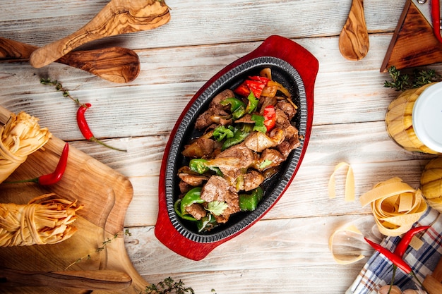 Vista superior de carne asada con verduras en sartén de hierro fundido sobre la mesa de madera