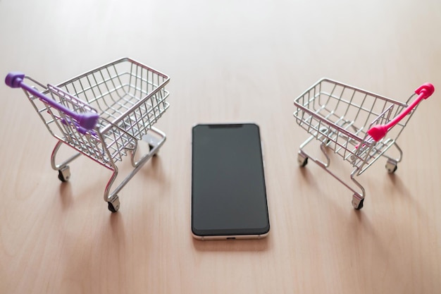 Vista superior en un carrito de compras y teléfono móvil en una mesa de madera Compras en línea de teléfonos inteligentes Compras en línea