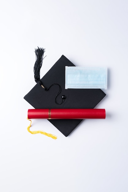 Foto vista superior del casquillo académico cuadrado de graduación con diploma de grado y máscara aislada sobre fondo blanco de mesa.