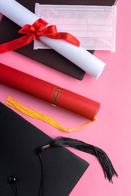 Foto vista superior del casquillo académico cuadrado de graduación con diploma de grado y máscara aislada sobre fondo de tabla rosa.