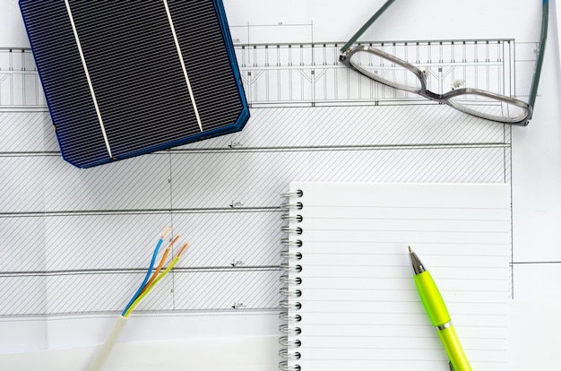 Foto vista superior de células solares, bloc de notas, bolígrafo, anteojos y cable eléctrico como concepto de planificación para proyecto fotovoltaico