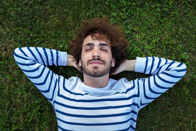 Vista superior de cerca de un joven sereno y relajado acostado en la hierba con los ojos cerrados