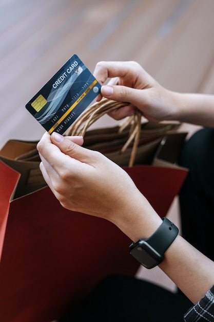 Foto vista superior, cerca de la mano de mujer joven con tarjeta de crédito en mano con bolsa de compras