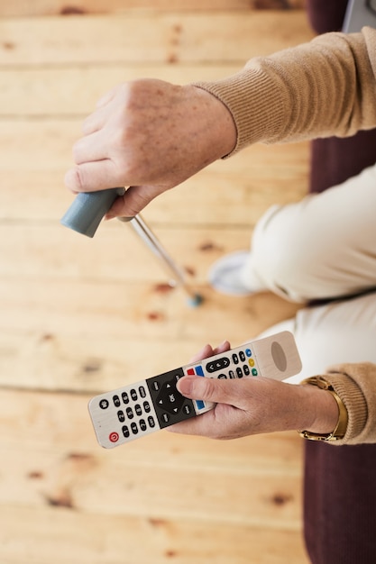 Foto vista superior de cerca de la mujer mayor caucásica sosteniendo el control remoto mientras ve la televisión en un hogar de ancianos, espacio de copia