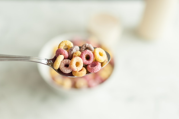 Vista superior del cereal de desayuno colorido brillante en un tazón con cuchara sobre fondo blanco.