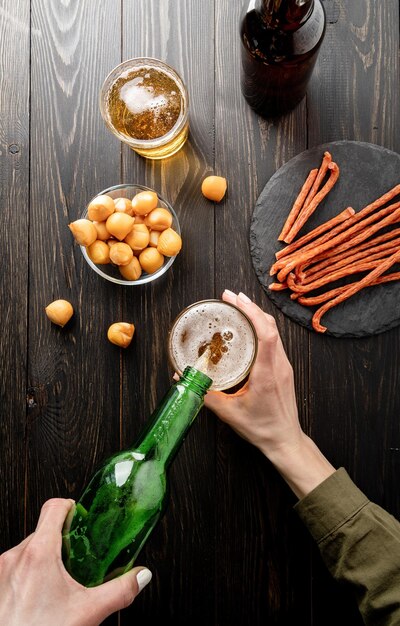 Vista superior de la cerveza que se vierte de la botella en el fondo de madera negra del vidrio