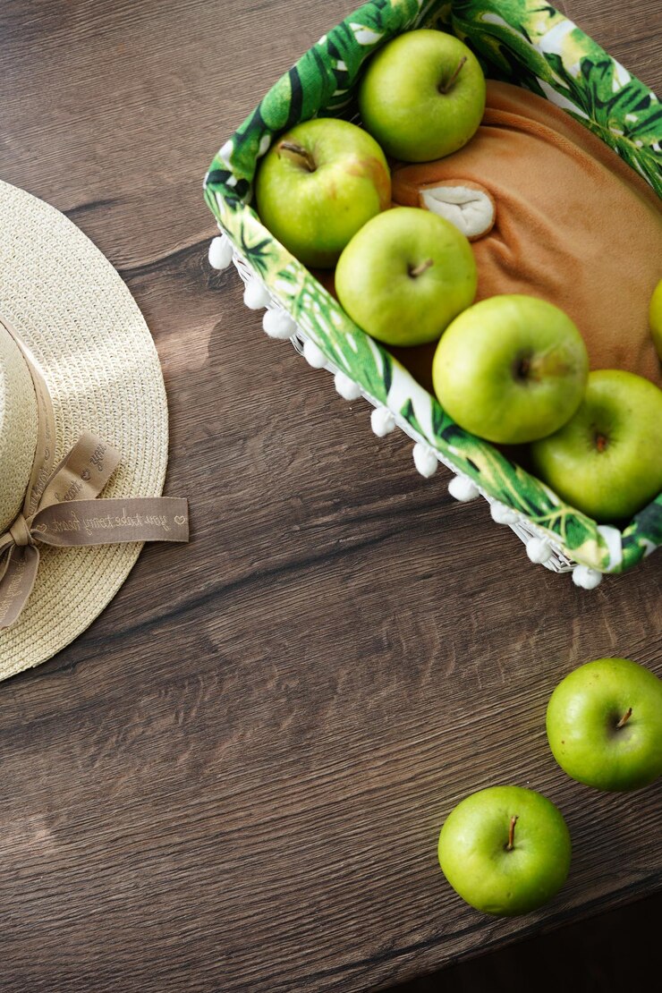 Una vista superior de una cesta de mimbre blanca con manzanas verdes y jugosas sobre una mesa de madera cerca de la ventana.