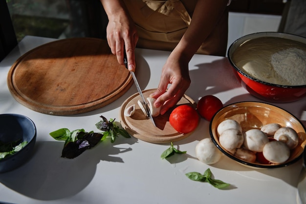 Vista superior Chef manos cortando champiñones en tabla de cortar de madera Los ingredientes para cocinar pizza están en una mesa de cocina