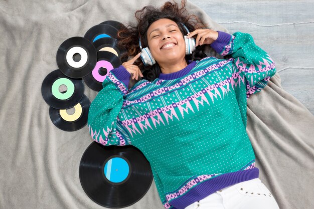 Foto vista superior de la chica latina tendida en el suelo escuchando música con discos de vinilo a su alrededor.