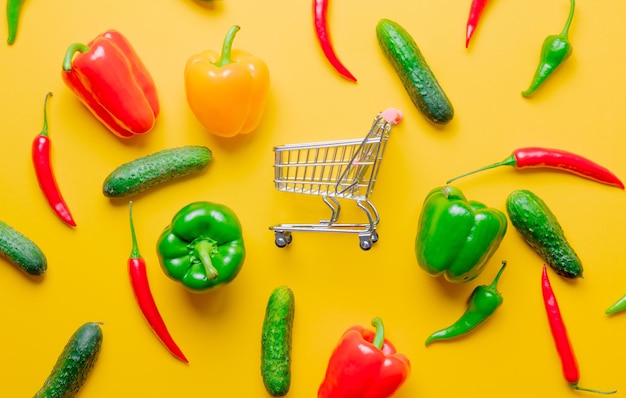 Vista superior en Chili pepper y pepinos con carrito de compras sobre fondo amarillo