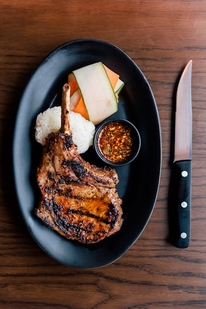 La vista superior de la chuleta de cerdo del Bbq del estilo tailandés sirvió con arroz pegajoso, la zanahoria cortada y la salsa picante tailandesa.