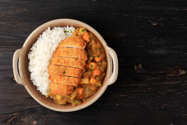 Vista superior de chuleta de pollo al curry con arroz - estilo de comida japonesa. Vista superior en placa de cerámica, mesa de madera negra con dados de patata y zanahoria, espacio para copiar texto