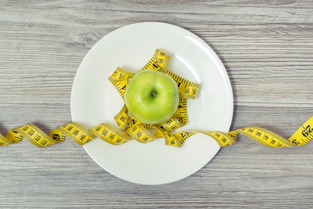 Vista superior de la cinta métrica enrollada alrededor de una manzana en un plato blanco