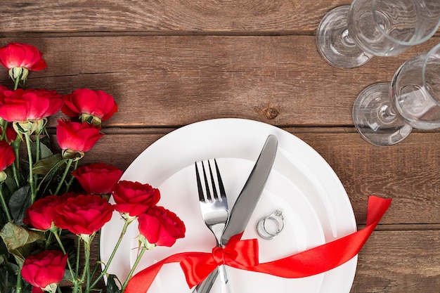 Vista superior closeup de jantar romântico servindo com um buquê de rosas vermelhas e anel acima da placa branca. Natureza morta